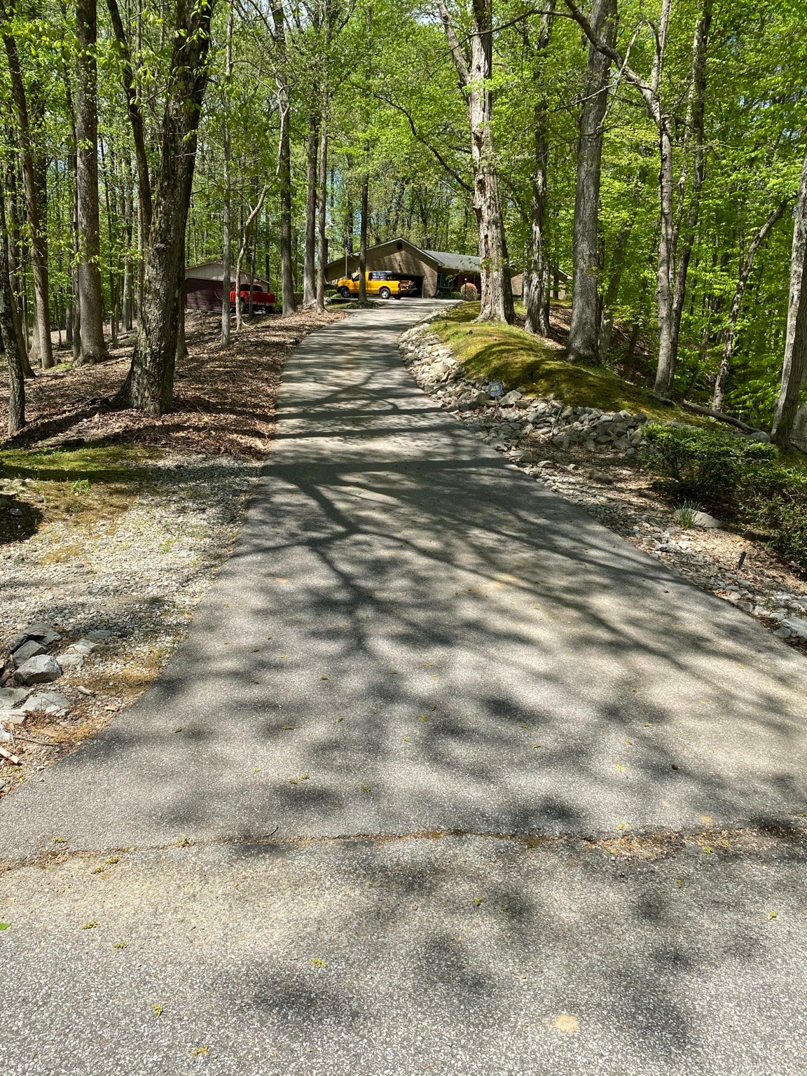 Wooded sloped asphalt driveway before sealcoating in Henderson County